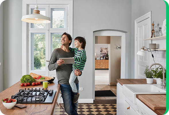 Père avec son enfant dans une cuisine lumineuse, regardant une tablette, illustrant la gestion de la consommation d’énergie à domicile.