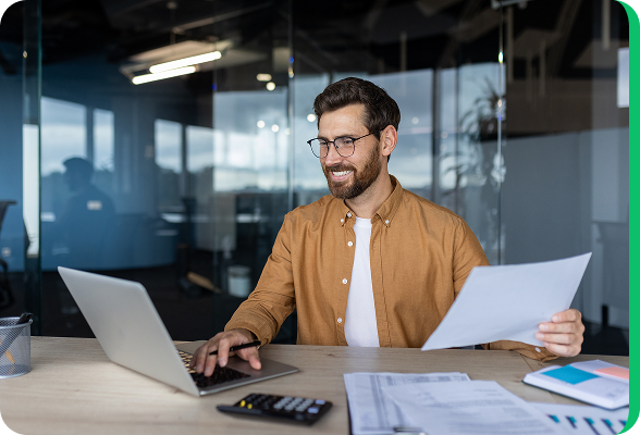 Homme souriant travaillant sur un ordinateur portable dans un bureau moderne, comparant des offres d’énergie en ligne.
